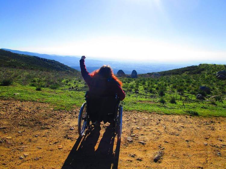 VIky in sedia a rotelle sulla cima di una montagna che alza il braccio in segno di vittoria